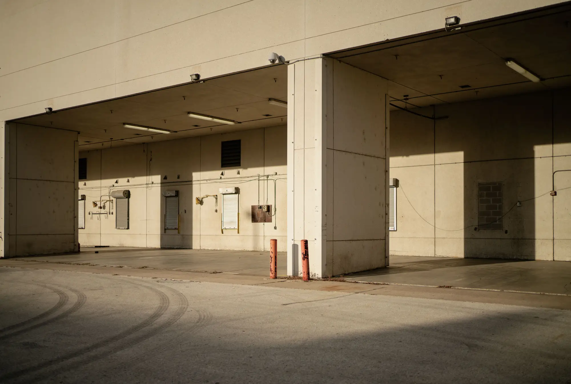 An empty loading dock in low sun, bays open and no trailers at the doors, tire marks across the apron
